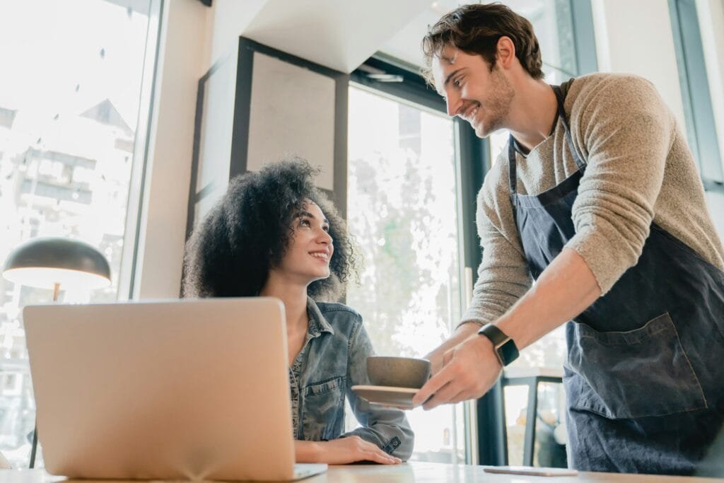 young-handsome-waiter-servicing-black-girl-customer-with-laptop-in-cafe-1024x683